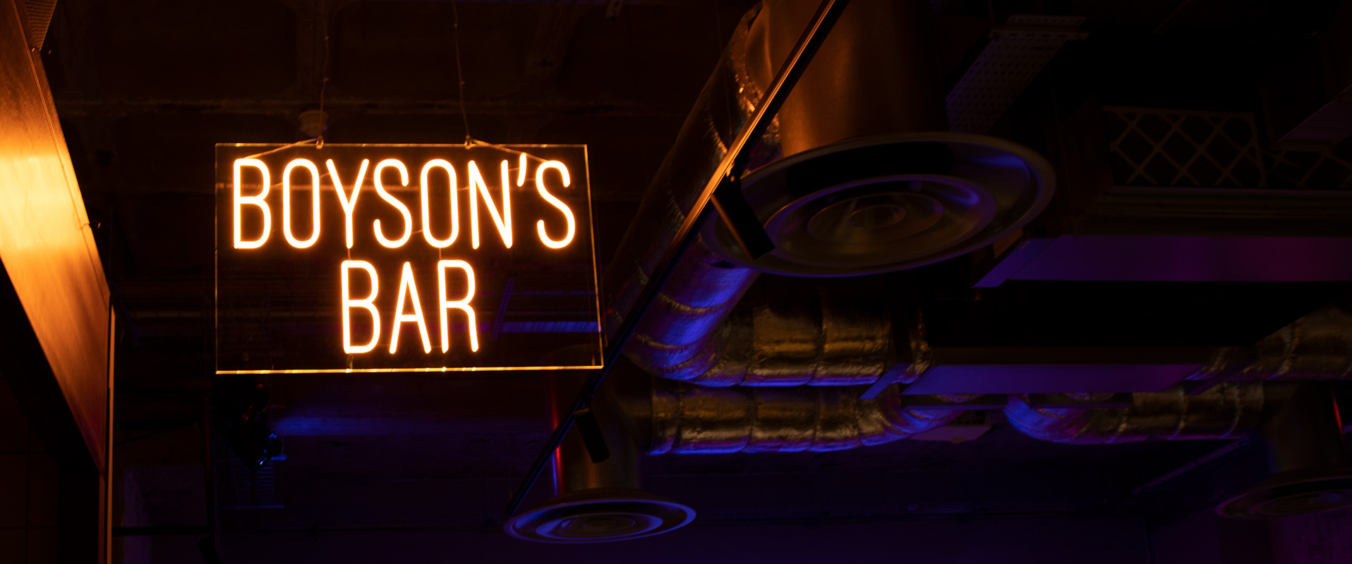 Picture of orange faux LED neon signage with the words: "Boyson's bar" hanging on the ceiling